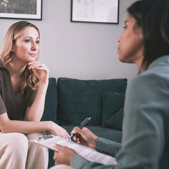 A community wellness professional holding a clipboard surveys a serious woman.